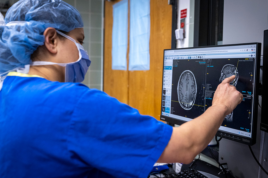 Dr. T. Purzner in surgical attire pointing to a brain scan displayed on a computer monitor.